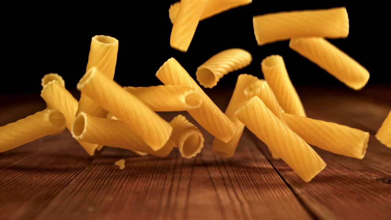 Rigatoni crudi che cadono su un tavolo di legno al rallentatore