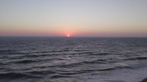 Gorgeous-Orange-and-Pink-Sunset-in-Oxnard,-California---4K-Drone-over-the-Ocean-Rapid-Pull-Back-to-Reveal-the-Sandy-Coast-and-People-Walking-Down-the-Beach