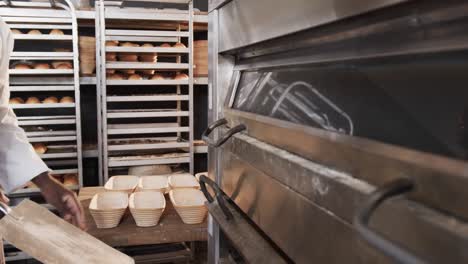 Happy-african-american-male-baker-working-in-bakery-kitchen,-putting-bread-into-oven-in-slow-motion