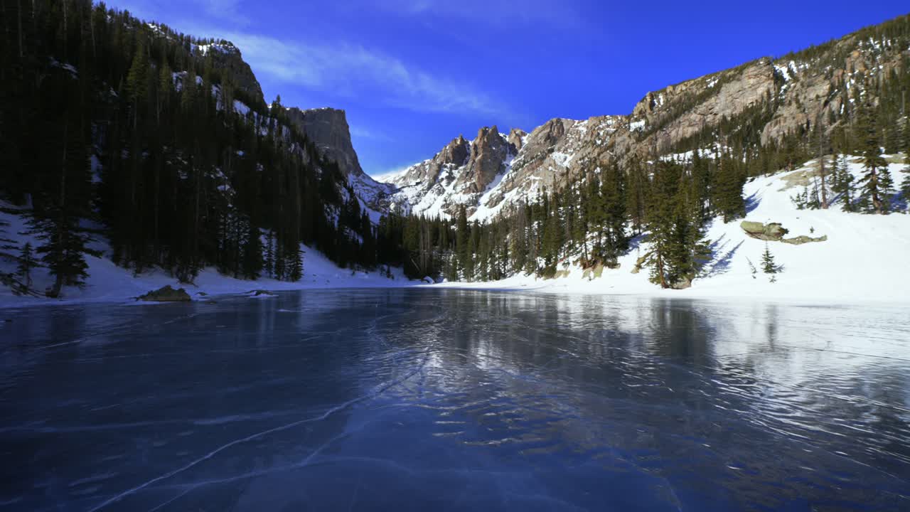 Paesaggio invernale del Lago dei Sogni con ghiaccio cobalto blu intenso nel Parco Nazionale delle Montagne Rocciose (RMNP), Colorado. Vista del paesaggio ghiacciato del Lago Smeraldo in alta montagna, sentiero del Bear Lake, con il picco Hallett sotto un cielo azzurro e soleggiato e le Montagne Flattop, con movimento di zoom.