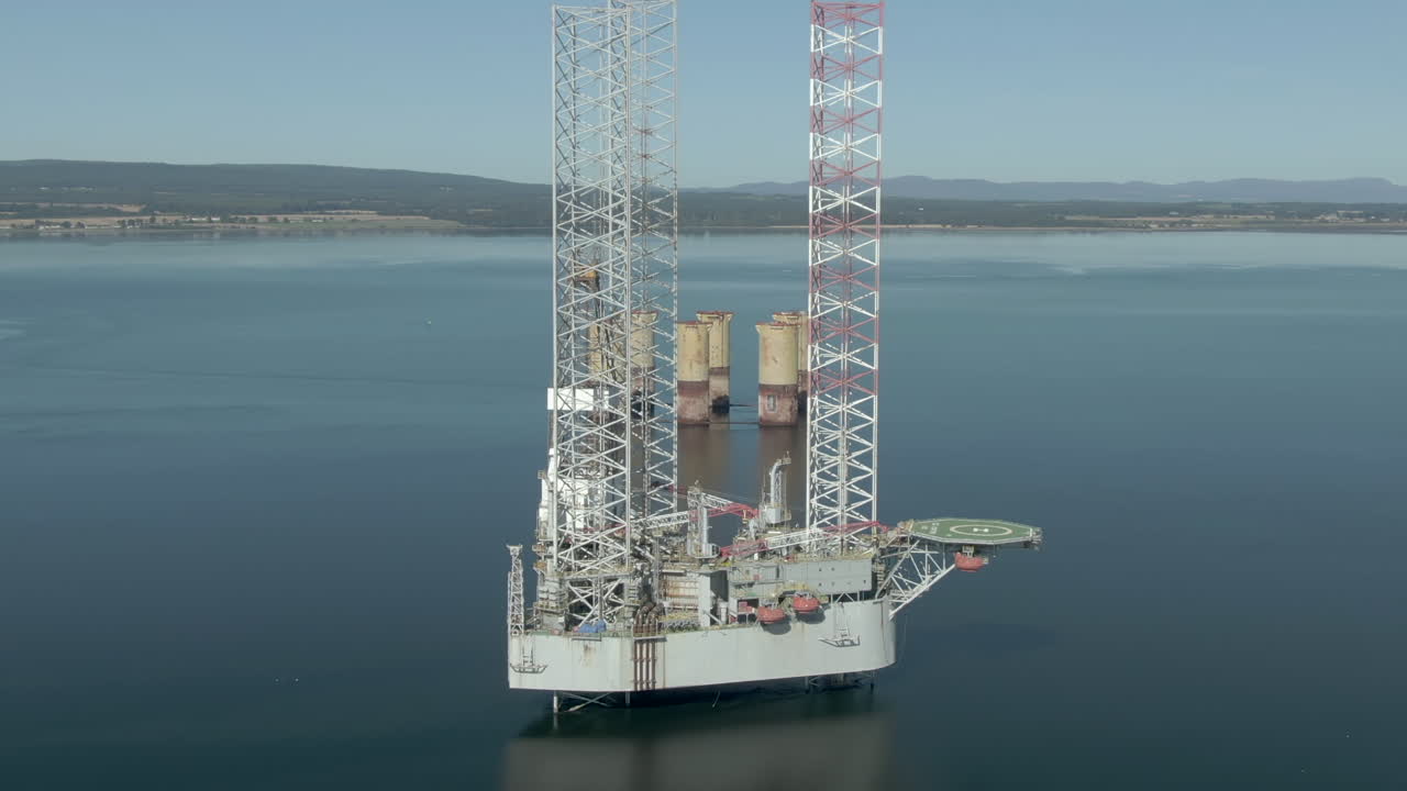 An aerial view of an oil rig on the Cromarty Firth on a sunny summer's day. Rotating anti-clockwise around the rig with zoom out.