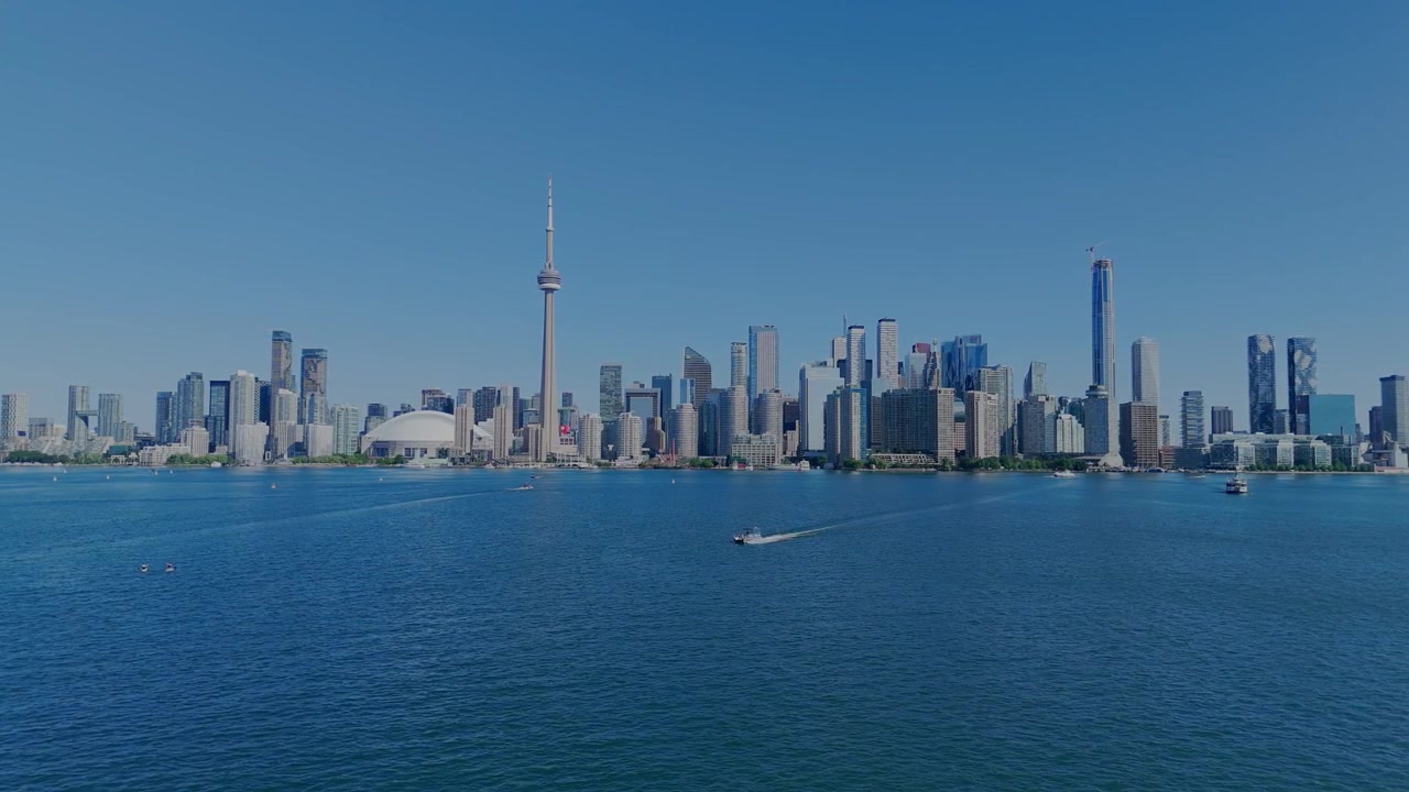 Cielo azzurro limpido sopra lo skyline della città. L'acqua luccica sotto lo sguardo luminoso del sole. Le torri della città si ergono alte, fiere e robuste. Una torre si innalza più alta, una sentinella orgogliosa. Piccole imbarcazioni scivolano sulle acque calme.