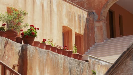 picturesque-potted-plants-with-red-and-green-flowers-in-quiet-and-peaceful-mediterranean-old-church,-Orthodox-monastery-Agia-Triada,-Crete-Greece