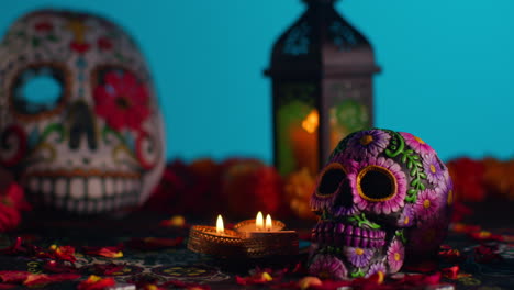 close up of decorated skulls and masks surrounded by candles and flower petals celebrating mexican holiday of dia de muertos or day of the dead against blue background