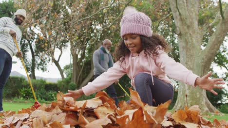 video of happy african american father and daughter collecting leaves with grandfather in garden