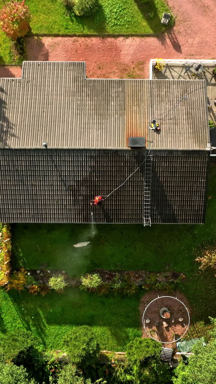 Aerial portrait on top of a woman pressure washing a house roof, sunny, fall day