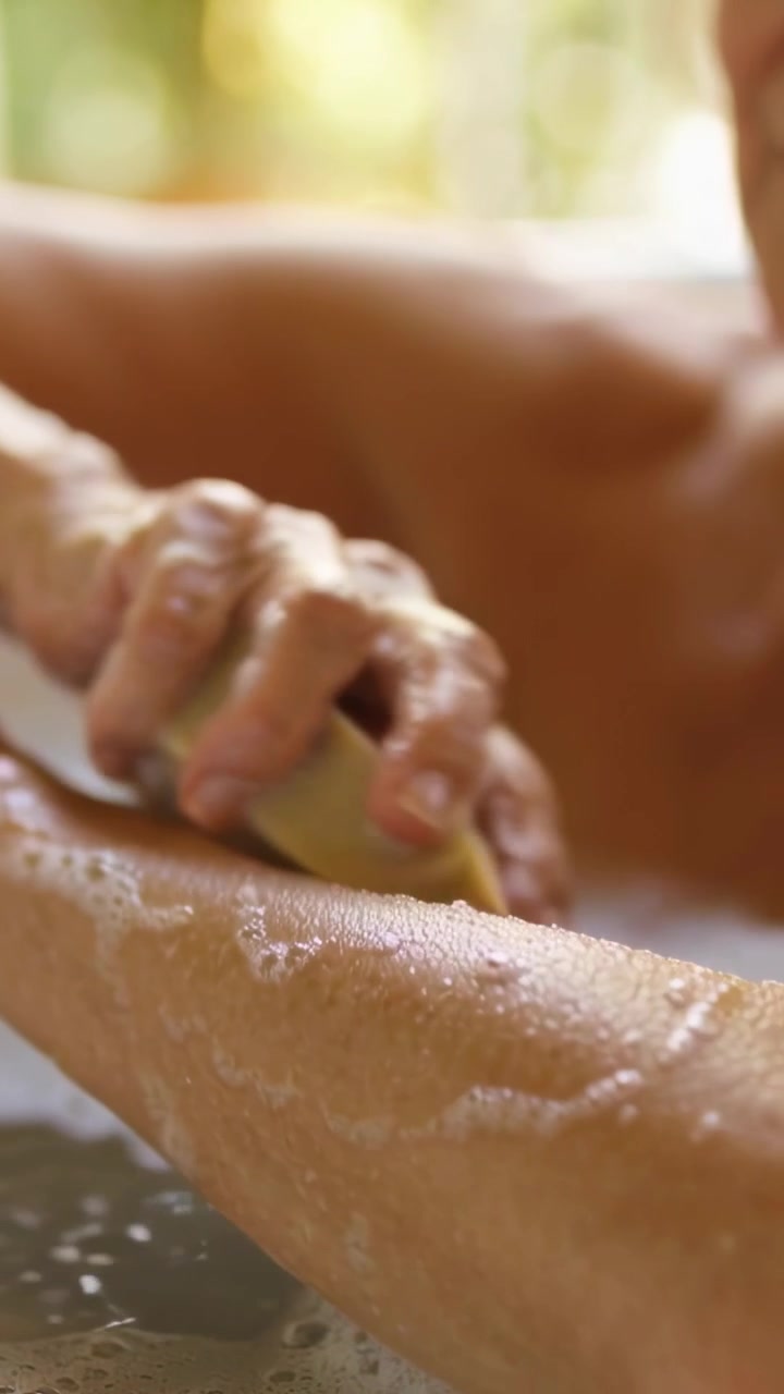 Video verticale: Donna che preme una saponetta, insapona l'avambraccio nella vasca da bagno pulendo la pelle a torso nudo