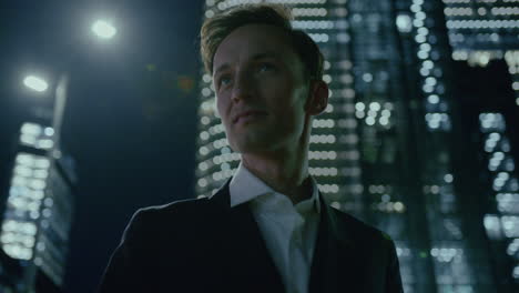 handsome executive young manager standing at night in modern illuminated city