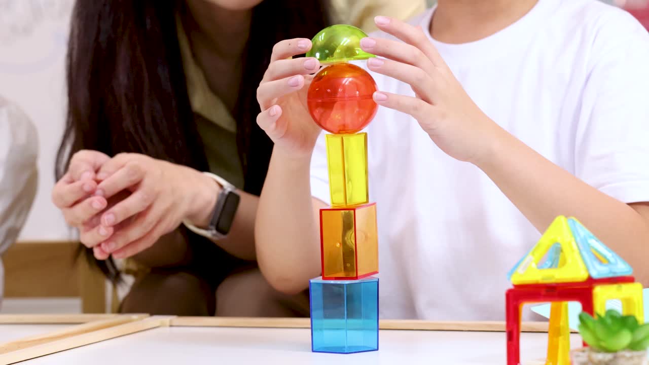 Child carefully stacks colorful blocks as teacher encourages, bright classroom lighting, static camera angle