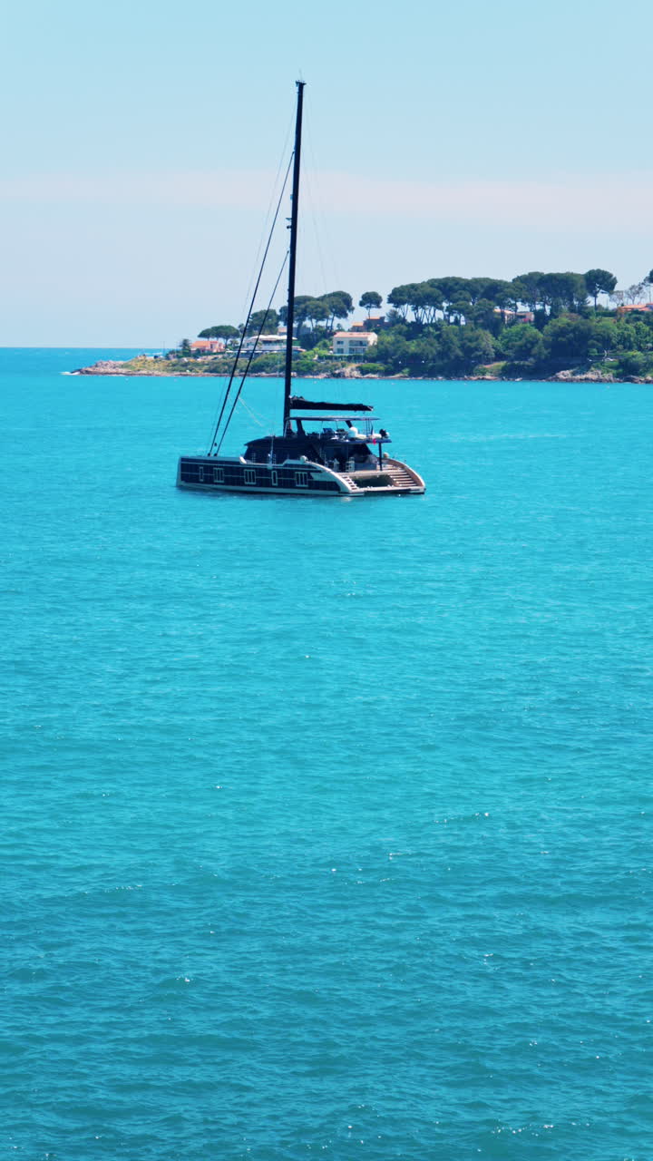 Boat floating on the Mediterranean sea with villas surrounded by greenery in the background. Vertical