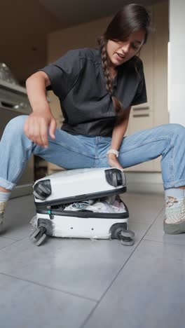 una mujer luchando para abrir una maleta dañada en una cocina.