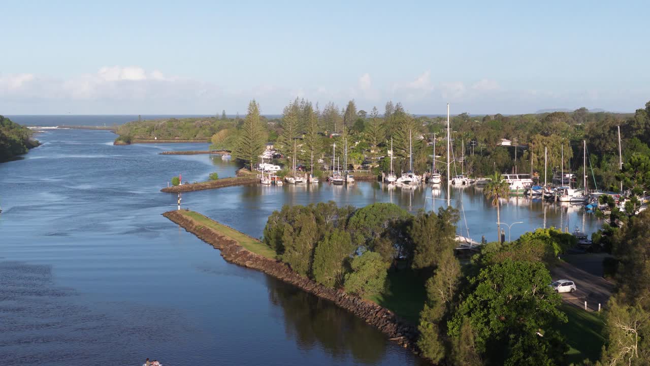 Aerial footage captures Brunswick Heads marina and river under clear skies, showcasing boats, lush greenery, and tranquil waters