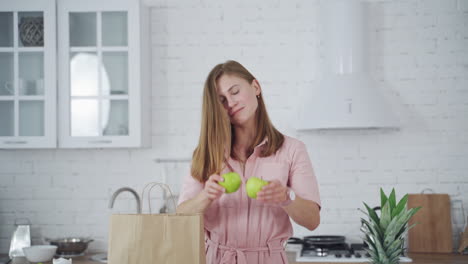 beautiful woman holding green apples on kitchen background. happy female closing her eyes by two fresh apples indoors. dieting concept. vertical video