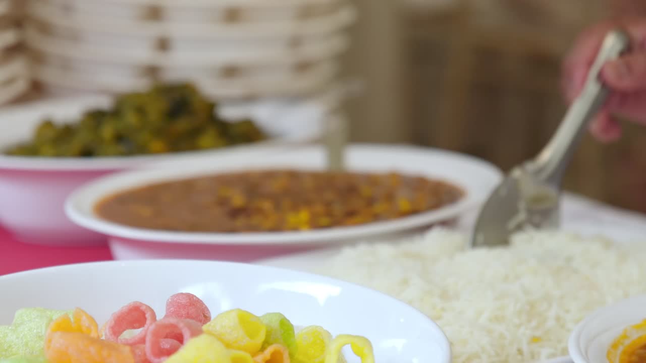 Medium shot of an Indian wedding buffet table featuring white rice, dhal, fryums, and bean stew served in bowls. A colourful and inviting display of authentic Indian cuisine