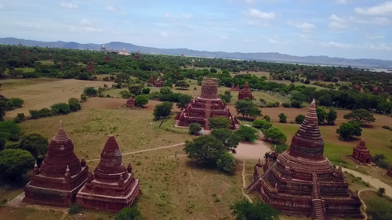 A wide dolly forward drone shot establishes a panoramic view of the temples in Bagan, Myanmar, blending red brick structures with lush green surroundings. A vivid scene of history and nature.