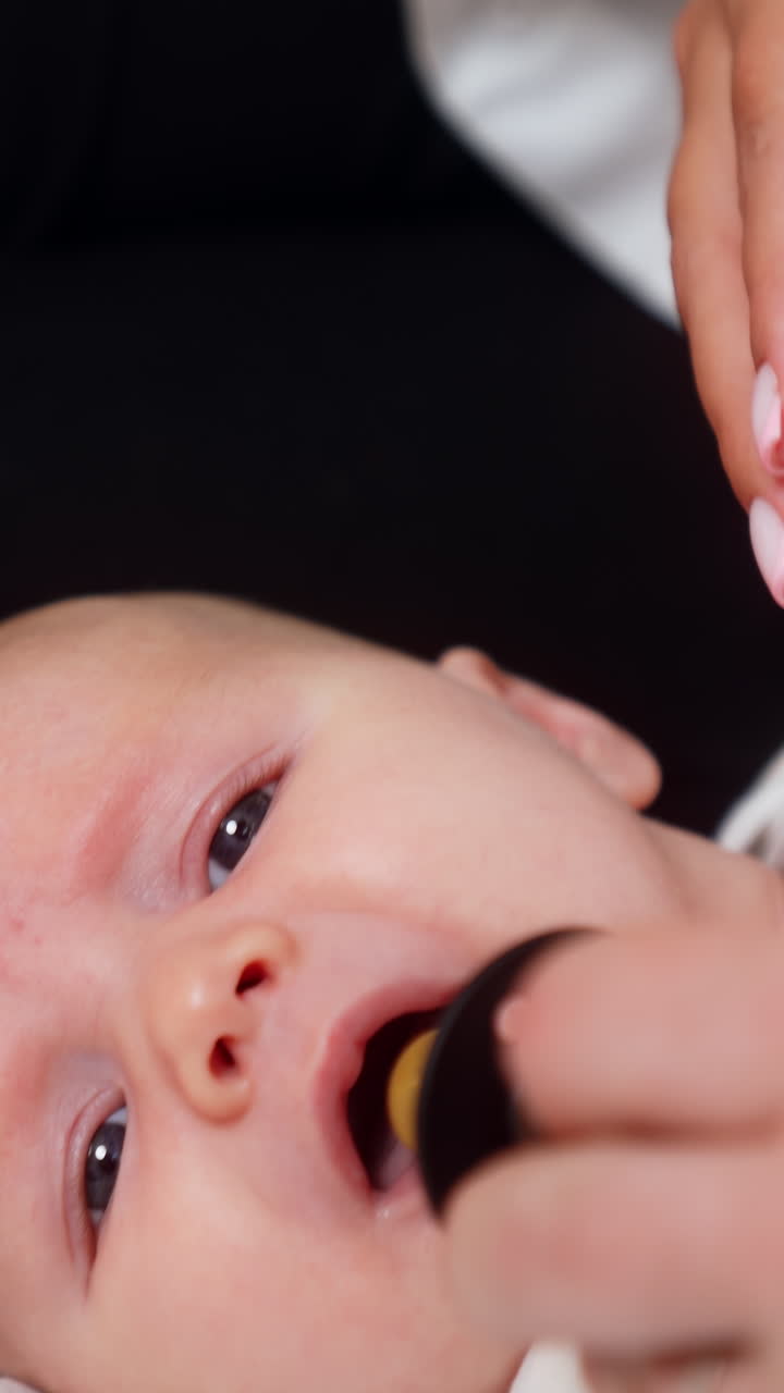 Little Caucasian newborn is going to cry. Baby lies on its back and tries to scream but mom gives him a pacifier. Close up. Vertical video
