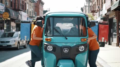 two individuals interact with a vibrant green and blue three-wheeled vehicle on a busy city street surrounded by shops and passersby