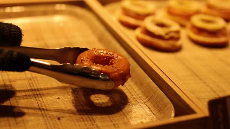 tongs lifting a donut off a baking tray