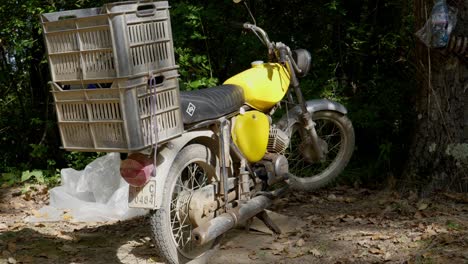 old dusty yellow motorbike with large crates tied to pillion hand held push