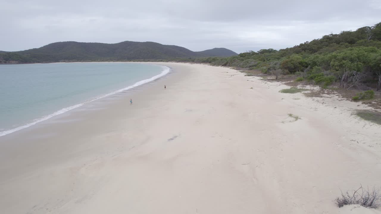 청록색 바다 파도가 해안에 튀는 하얀 모래 해변, 호주 퀸즐랜드 그레이트 케펠 섬의 해변에서 즐기는 커플 관광객 - 공중 드론 샷