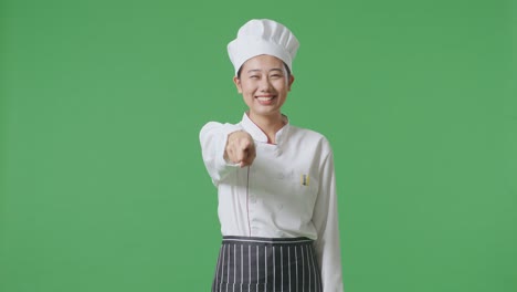 Asian Woman Chef Smiling And Touching Her Chest Then Pointing At You While Standing In The Green Screen Background Studio