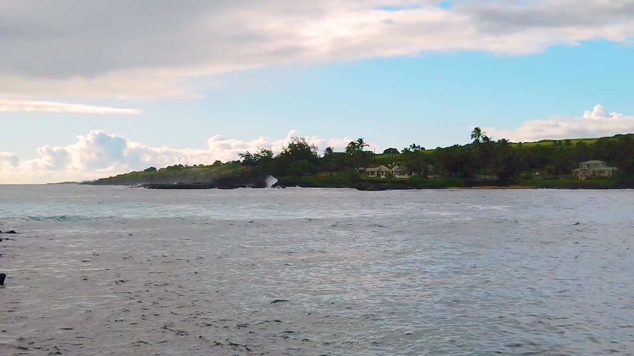 HD Hawaii Kauai static of ocean waves rolling in foreground from left to right as waves crash and Spouting Horn blowhole goes off in distance with last spout going above hillside in background