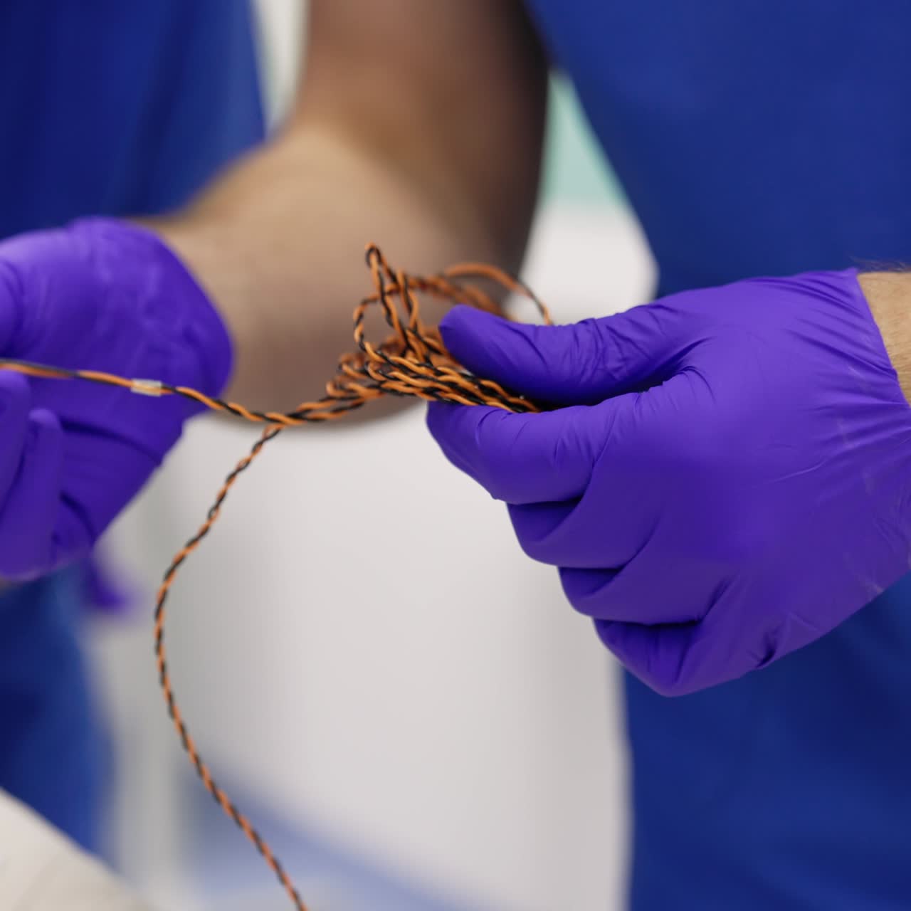 Mani maschili con guanti in lattice districano il cavo nero e giallo di un'apparecchiatura. Preparazione per il neuromonitoraggio di un paziente. Primo piano