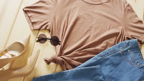 video of close up of brown t-shirt, denim jeans and sunglasses on wooden background