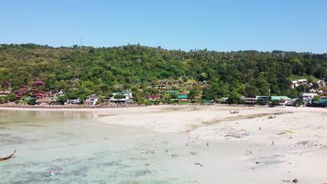 colorful village in phi phi don island with people on beach shoreline and forest at background
