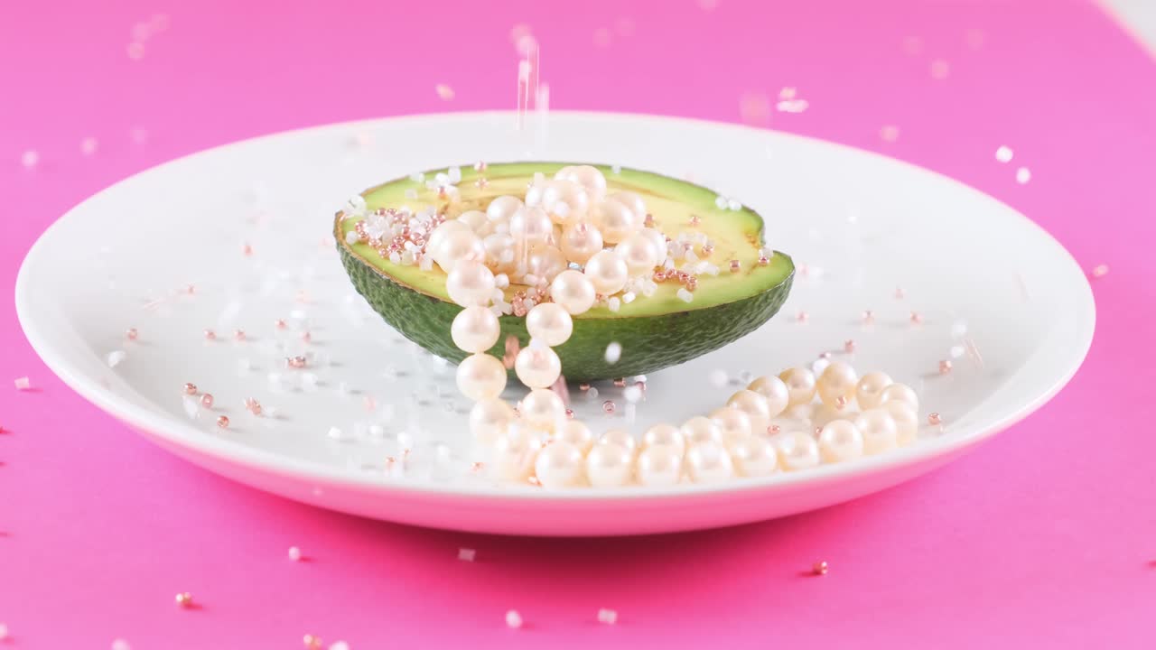 분홍색 배경에 rhinestones로 인 색 접시에 진주와 함께 반 신선한 아보카도