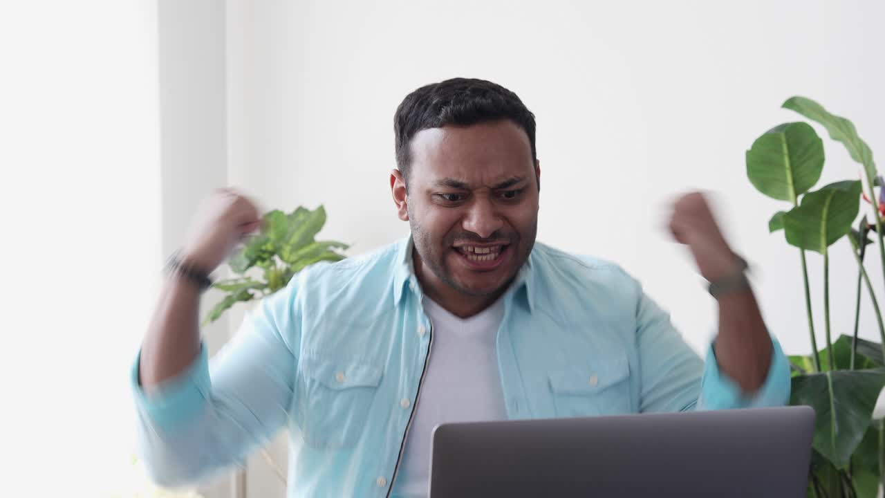 Young indian man student or freelancer in casual clothes, feel euphoria, having received the good news on your laptop computer