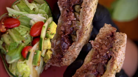 vertical slow motion of a person wearing black latex gloves holding and presenting a prosciutto with fig sauce and capers sandwich