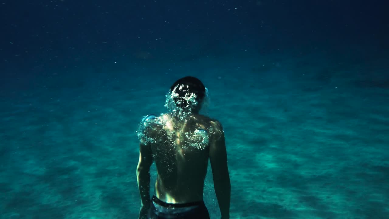 hombre delfín patea hacia la superficie y expulsa aire mientras se eleva