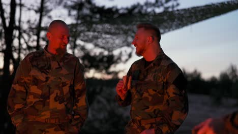 the military set up camp at night in the training areas, lit a campfire to warm up and frying sausages on sticks, the men were on duty, guarding the training ground, talking among themselves