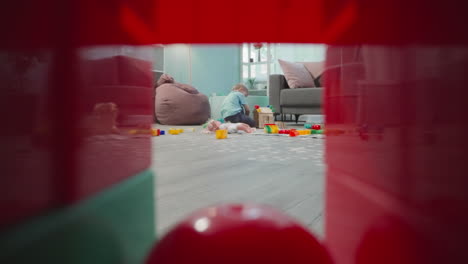 toddler builds house from blocks sitting on wooden floor