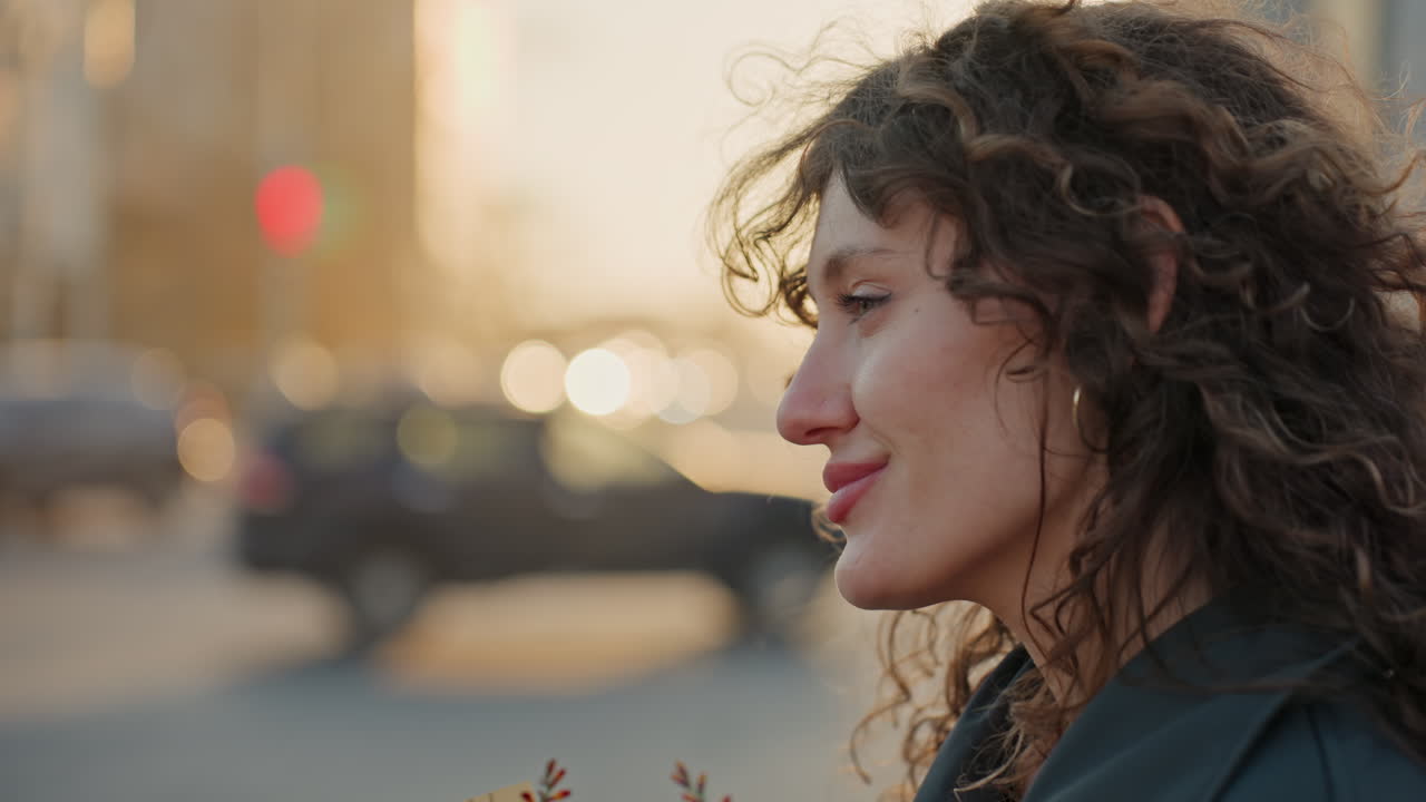 Ritratto ravvicinato di una fiorista con un bouquet in una calda luce cittadina, sfondo bokeh morbido, sguardo pensieroso e sorriso gentile, capelli ricci che catturano riflessi dorati, momento intimo di quieta speranza.