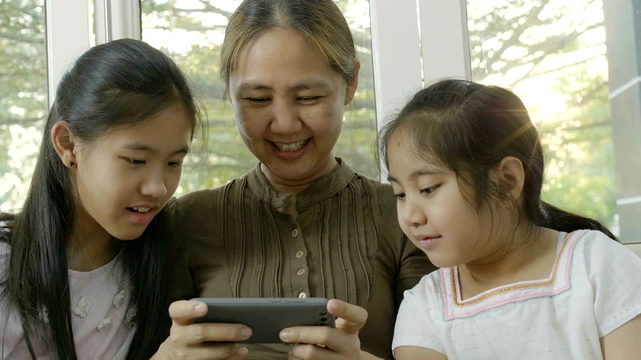 4k 아시아 여성이 딸들과 함께 스마트폰에서 게임을 하고 행복한 시간을 보내고 있습니다.