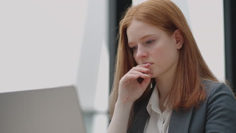 Una-Mujer-Pelirroja-Preocupada-Y-Reflexiva-Que-Trabaja-En-Una-Computadora-Portátil-Mirando-Hacia-Otro-Lado-Pensando-En-Resolver-Un-Problema-En-La-Oficina-Una-Mujer-Seria-Busca-Inspiración-Para-Tomar-Decisiones-Y-Sentir-Falta-De-Ideas