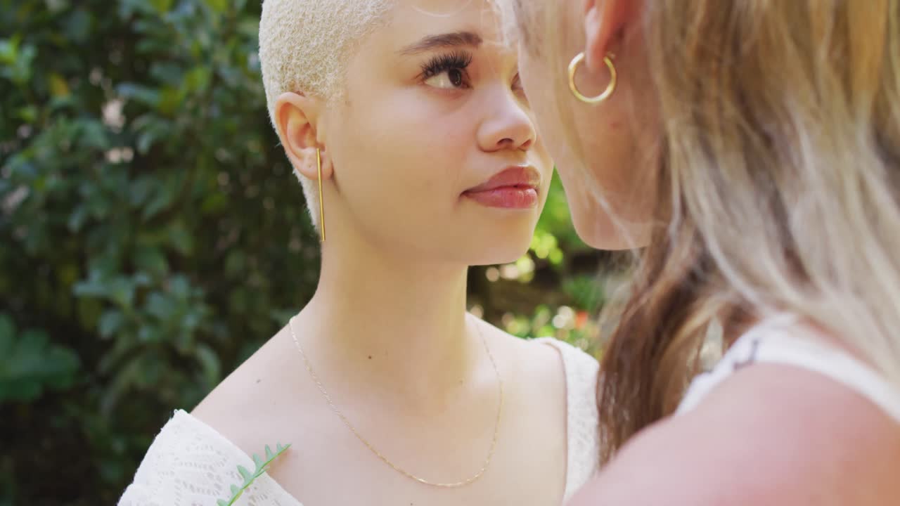 feliz pareja de mujeres diversas cogidas de las manos y tocando las frentes en el jardín