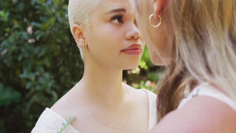 feliz pareja de mujeres diversas cogidas de las manos y tocando las frentes en el jardín