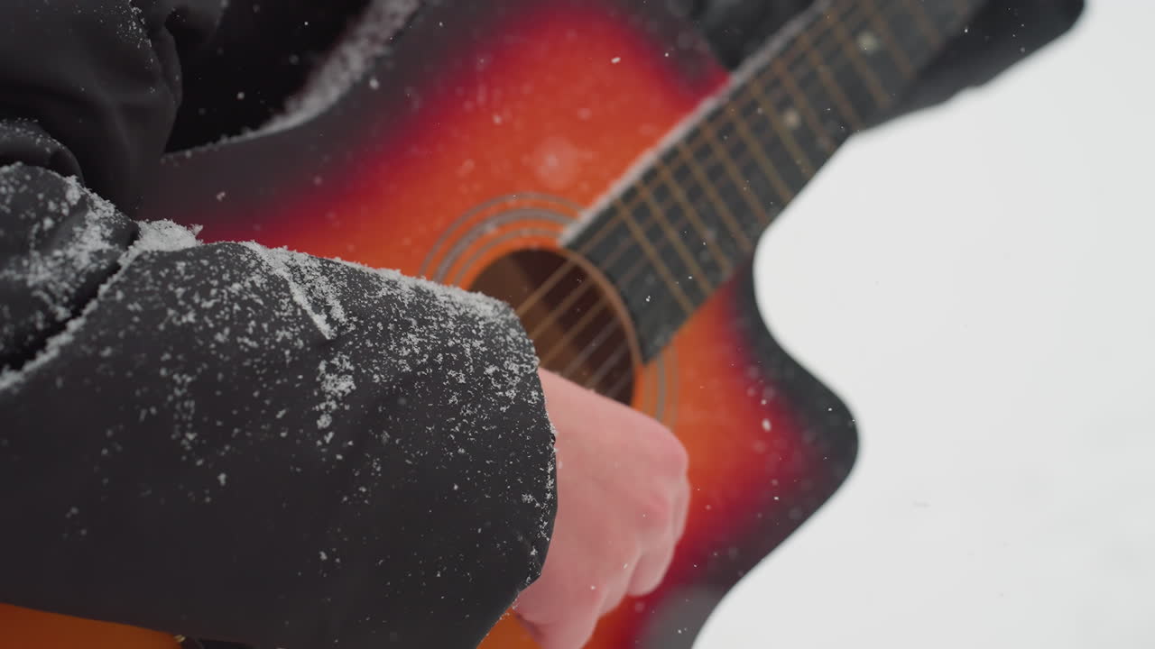 활기찬 빨간색과 오렌지색 음색으로 기타를 연주하는 손의 클로즈업, 눈으로 인 팔꿈치가 보이고, 음악과 겨울의 추위의 조화로운 혼합을 만니다.