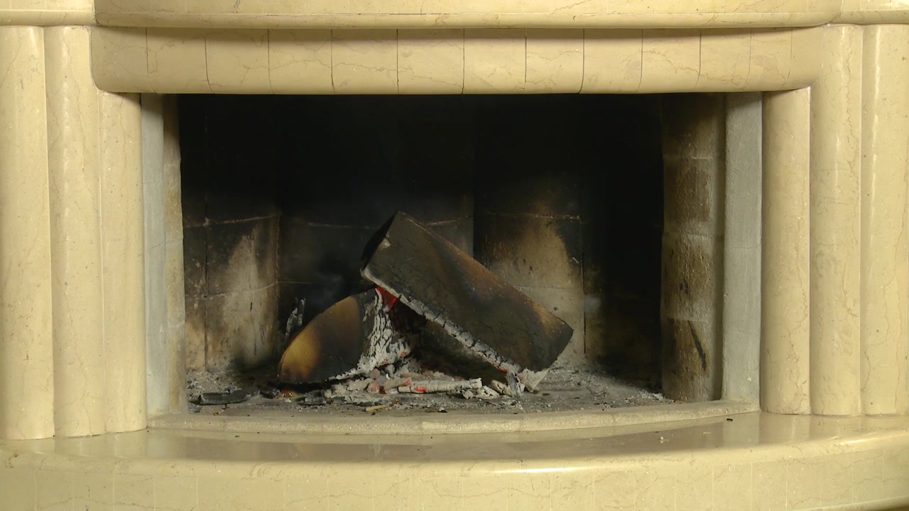 Toma estática amplia de leña humeante, ceniza y humo en una chimenea doméstica, simbolizando el calor que se desvanece y las relaciones que se enfrían