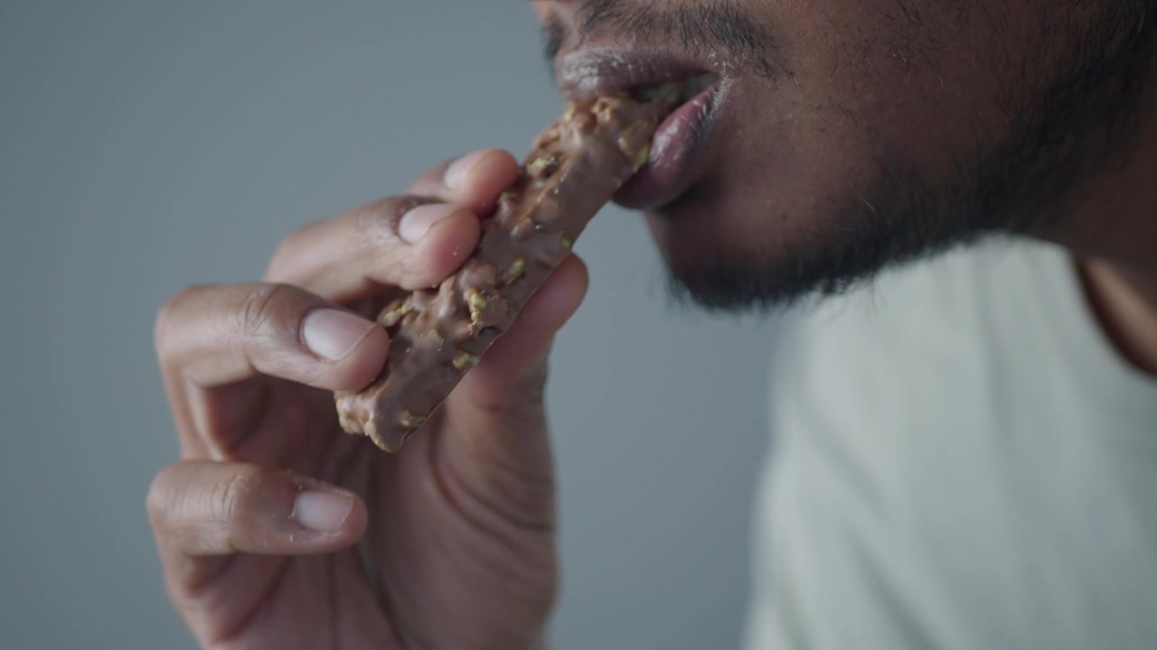Primer plano de un hombre comiendo una tableta de chocolate con frutos secos