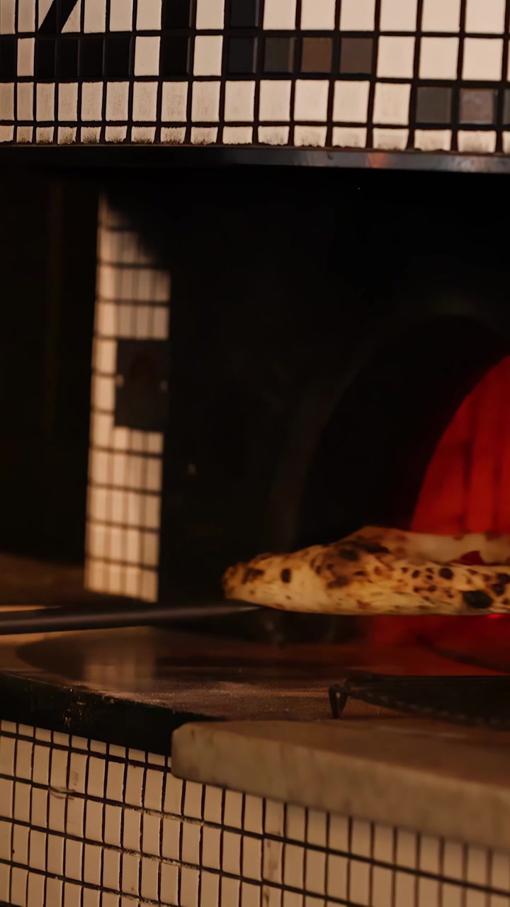 Uno chef rimuove una pizza fumante da un forno a mattoni incandescente in una cucina di ristorante.