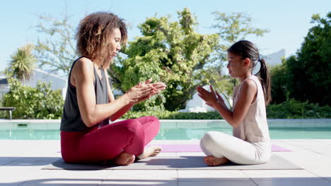 Feliz-Madre-Birracial-E-Hija-Practicando-Yoga-Sentadas-En-Un-Jardín-Soleado,-Cámara-Lenta