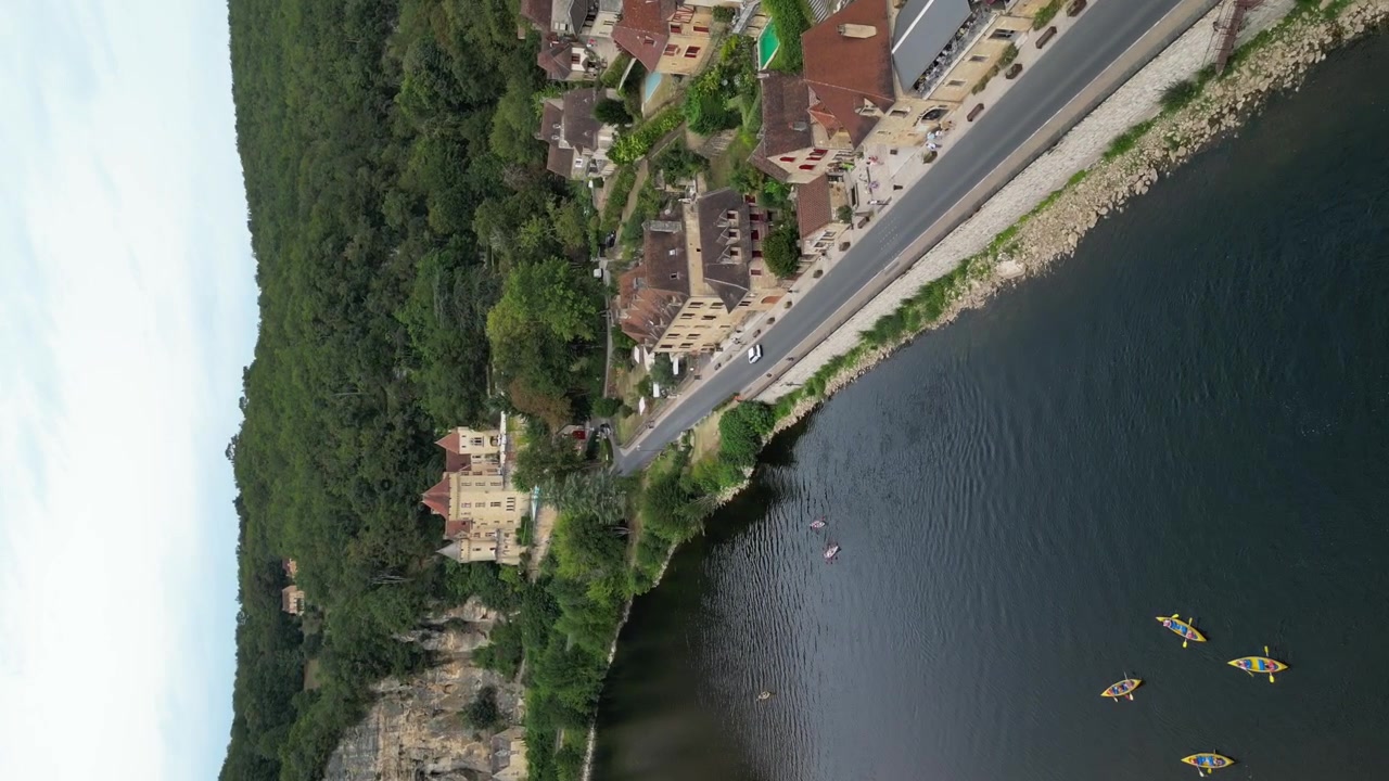Vista aerea con drone nella campagna francese di una piccola e antica città medievale sotto una falesia di pietra, circondata da una foresta verde e da un fiume che la circonda, a La Roque Gageac, vista verticale.