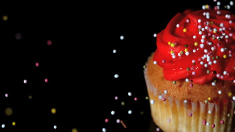 Colourful-sprinkles-pouring-onto-cupcake-on-black-surface