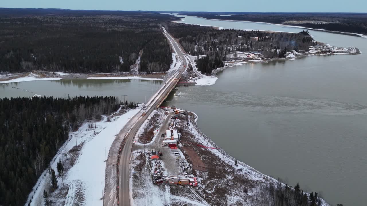 Kasım ayında, yerde kar varken Manitoba, Thompson yakınlarındaki Burntwood Nehri Köprüsü. Hava kamerası köprüye doğru kuzeye uçarak akan nehri ve otoyoldaki arabaları gösteriyor.