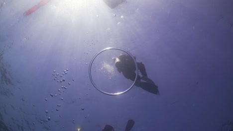 air bubble ring rising from scuba diver toward surface with sun and scuba divers in background at phuket, thailand