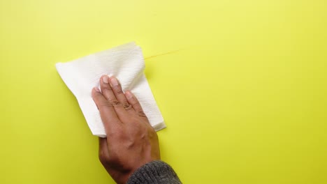 persona limpiando una superficie amarilla con una toalla de papel